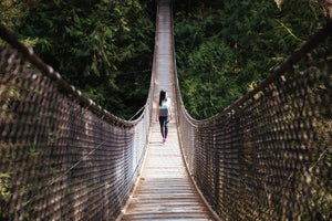 Woman crossing over a walking bridge in a dense forest.